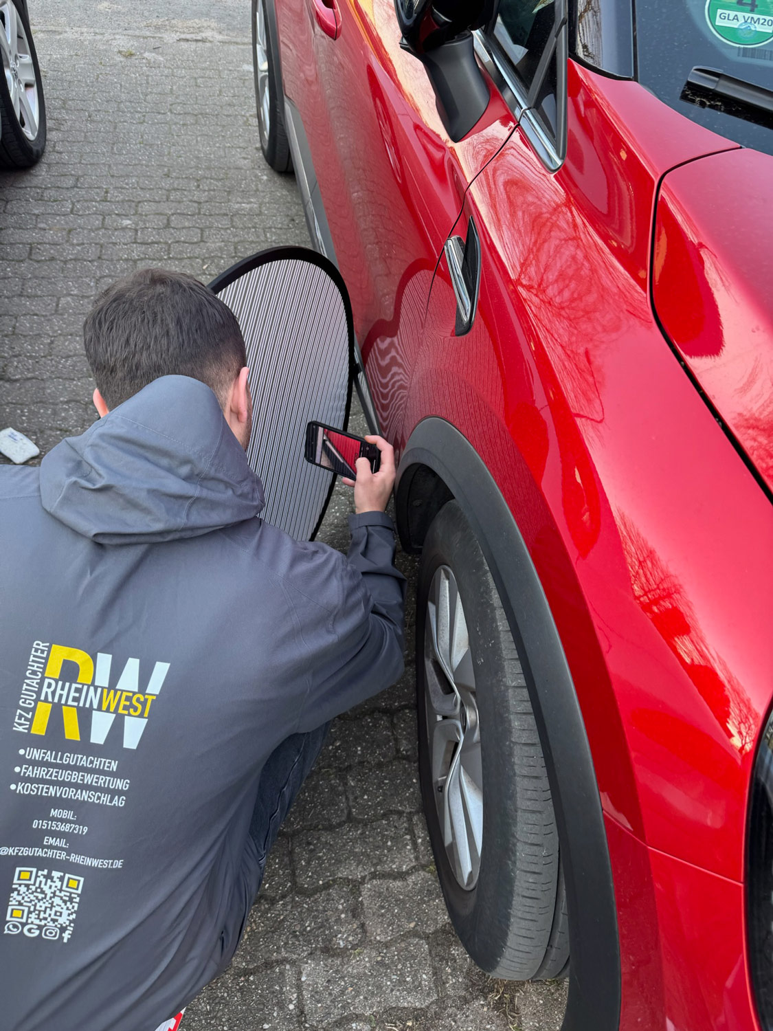 Ein Mann mit dunklem Haar fotografiert konzentriert ein rotes Auto am Hinterrad