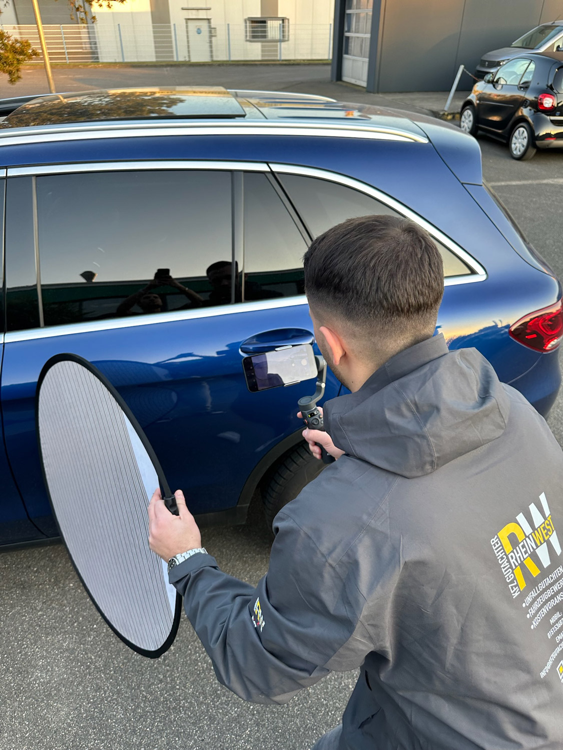 Ein Mann mit kurzem Haarschnitt prüft konzentriert den Lack eines blauen Autos