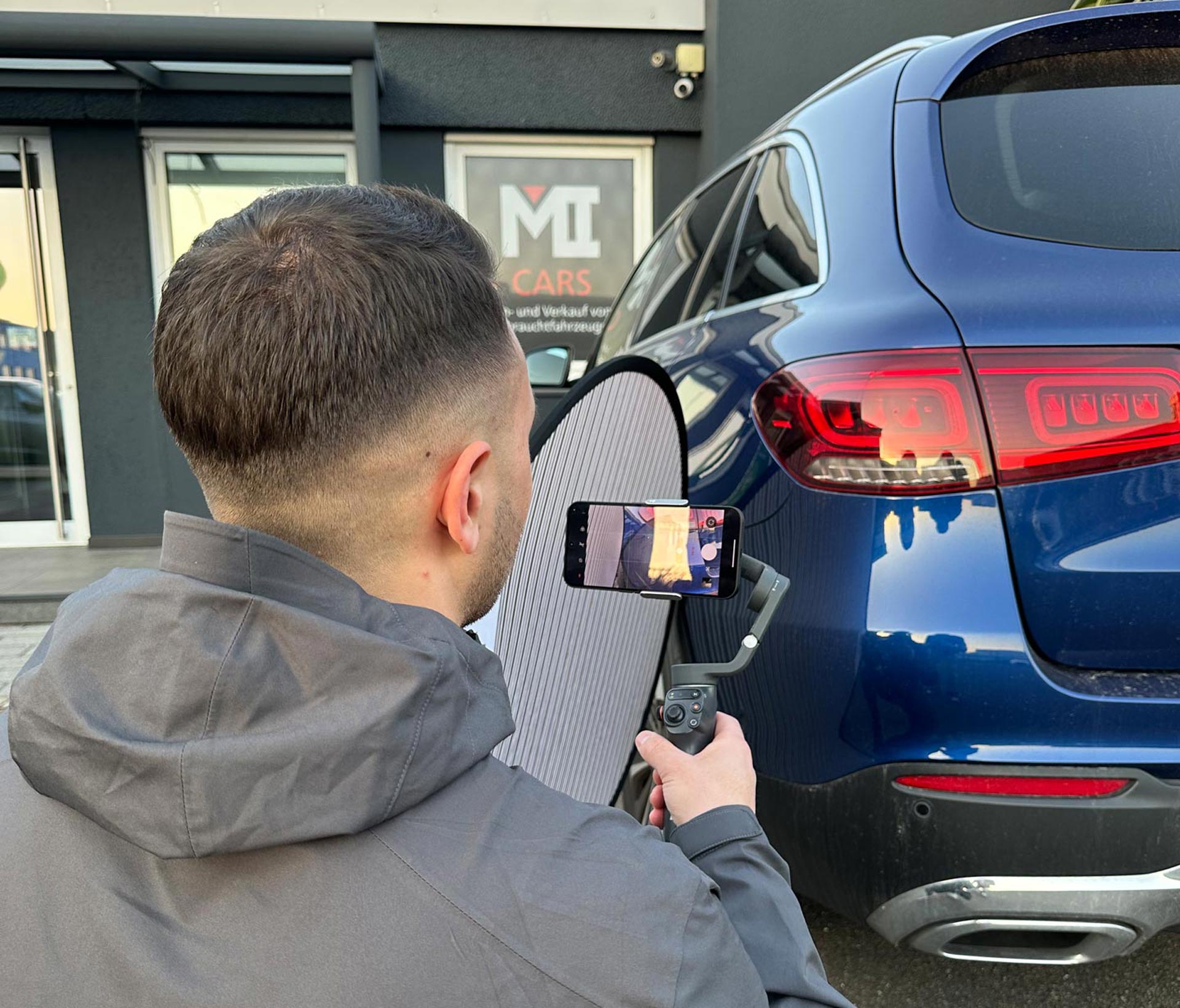 Ein Mann mit kurzem dunklem Haar filmt einen blauen SUV mit seinem Smartphone