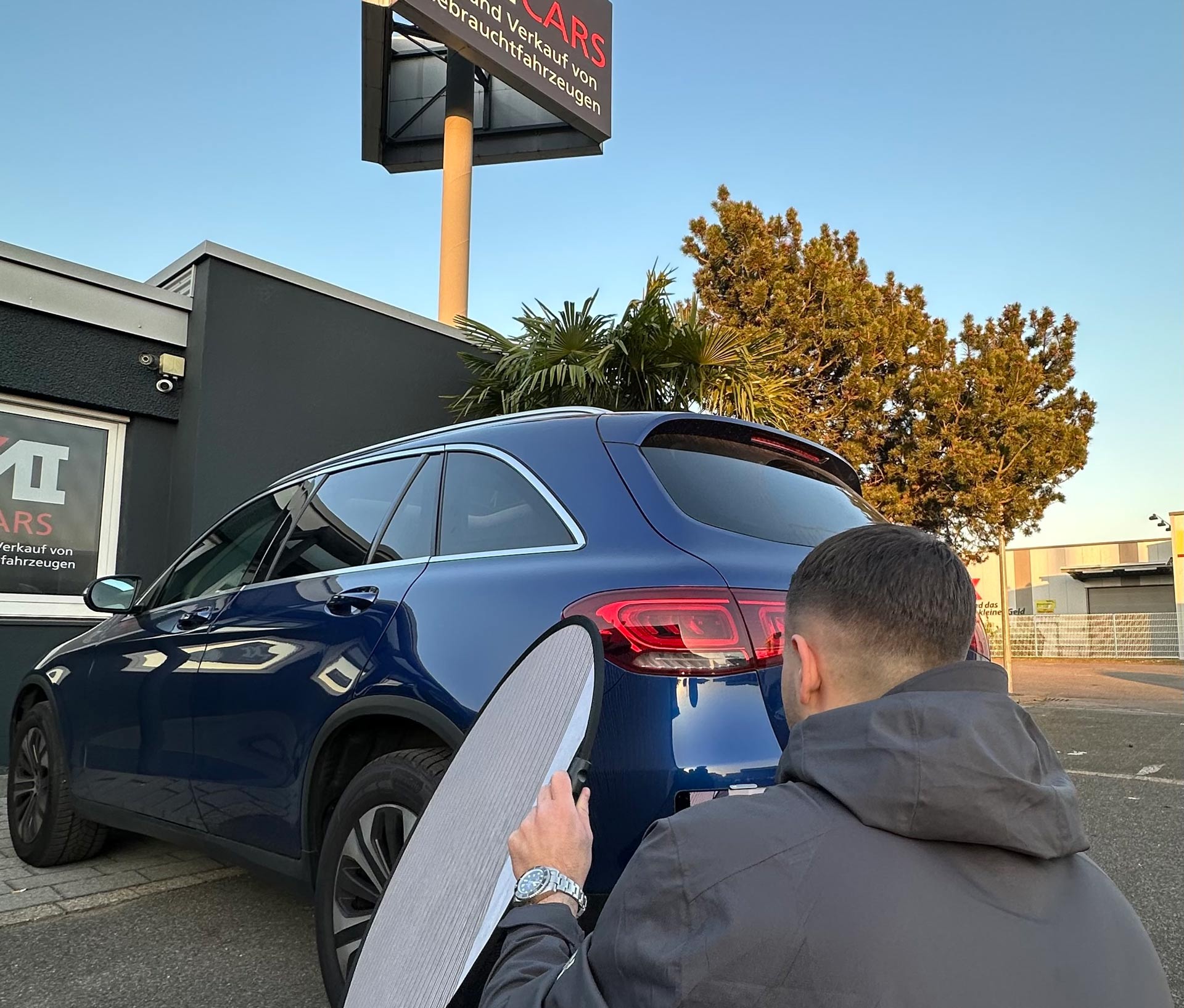 Ein Mann mit dunklem Haar reinigt konzentriert ein glänzend blaues Auto im Freien
