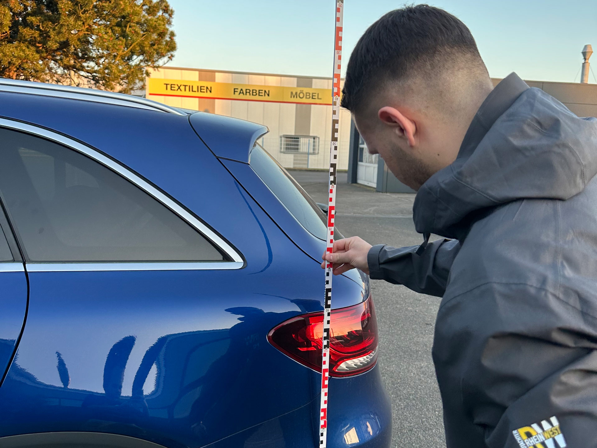 Ein Mann mit kurzem dunklem Haar misst konzentriert die Höhe eines blauen Autos